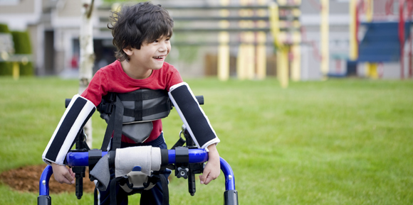 Disabled four year old boy standing in walker near a playground